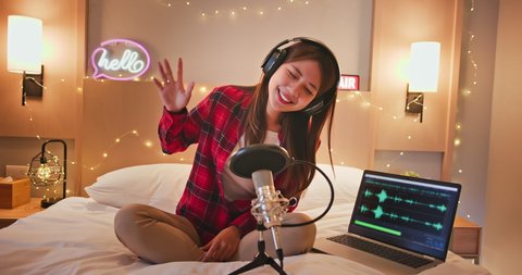 asian woman with microphone is singing and recording podcast in bedroom at home