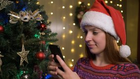 Portrait of young beautiful woman with santa hat in winter sweater typing message on mobile phone - Powered by Shutterstock - Get 15% off with code: PIKWIZARD15