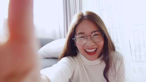 Lovely Asian woman wearing glasses is smiling and waving happy times to the video call for a selfie with a friend. Slow motion