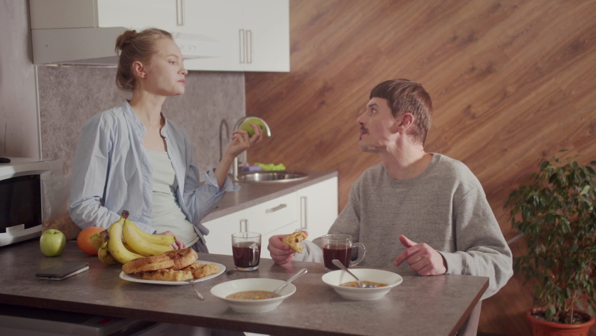 A happy family has lunch in the sunlit kitchen of their new home. A plate of soup, pies, fruit on the table. Communication between husband and wife.