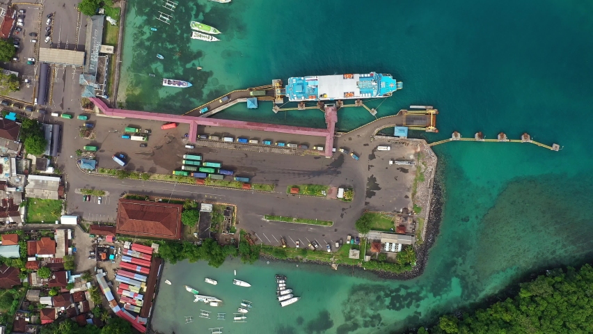 Top down aerial footage of trucks unloading from a ferry boat coming from Lombok in the Padang Bai harbor in Bali, Indonesia. Shot with a rotation motion. 
