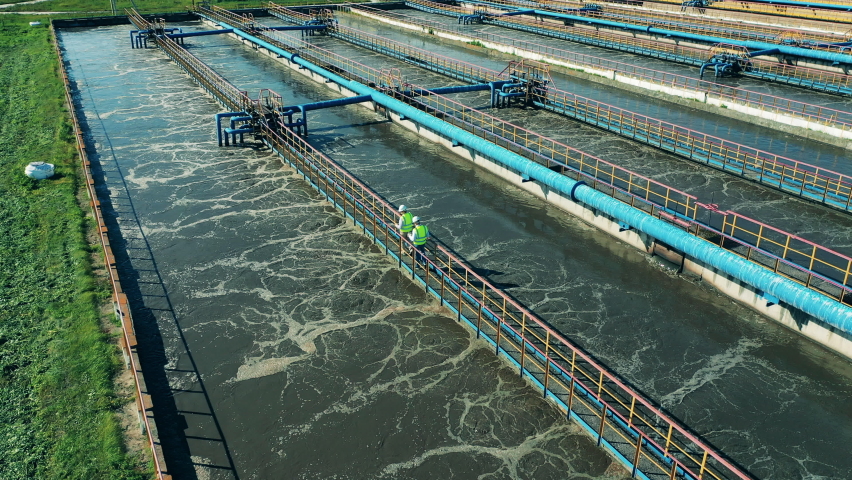 Two wastewater operators walking along the pipes at a sewage cleaning facility. Sewage treatment concept. | Shutterstock HD Video #1064401231