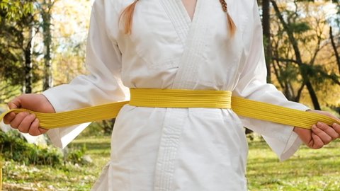 teenager girl 12 years old is engaged in karate outdoors in the park. Healthy lifestyle concept. playing sports. martial arts. Judo, Jiujitsu. bold, strong. ties a belt on a kimono