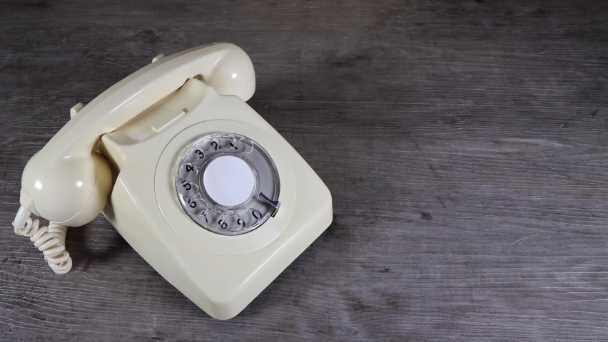 A elegant woman's hand picking up, putting down and flirting on an old vintage 70's and 80's style rotary telephone receiver on a wooden background, retro office phone call concept Royalty-Free Stock Footage #1064408563