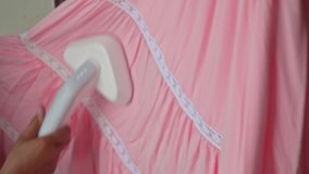 4K video of a woman's hand ironing a pink hanging dress with a steaming machine