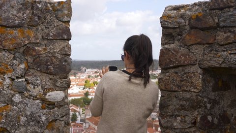 Caucasian woman photographing with cellphone city view of Montemor o Novo from the castle tower in Alentejo, Portugal