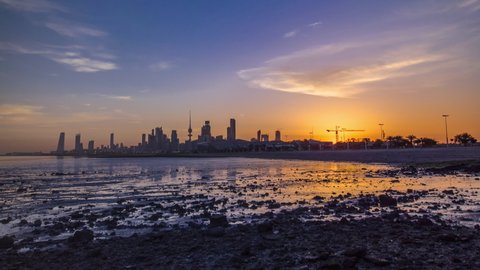 Seaside skyline of Kuwait city sunrise timelapse. Modern towers and skyscrapers reflected in water.