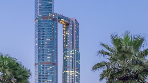 ABU DHABI, UAE - CIRCA APRIL 2019: Skyscrapers of Abu Dhabi illuminated with towers buildings day to night transition timelapse. Palms in park and street light