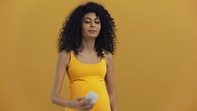 smiling bi-racial pregnant woman having video chat isolated on dark yellow