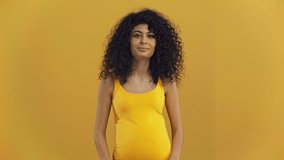 happy bi-racial pregnant woman showing romper isolated on dark yellow