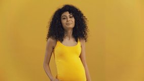 happy bi-racial pregnant woman taking gift box isolated on dark yellow