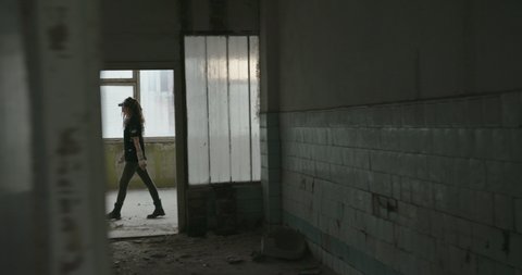 Glimpses of a woman in an abandoned building as she walks along a passage passing open doorways in an evocative concept