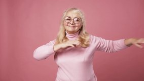 Active retirement. Positive happy senior woman in glasses dancing over pink studio background, fast motion