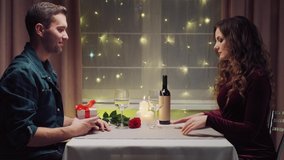 A handsome brunette man gives his beloved a gift in a white box with a red bow. Romantic dinner. Valentine's Day.