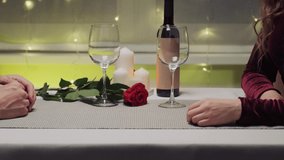 Men's hands are stroking the hands of the woman they love. Without a face. A table with a bottle of wine and candles. Romantic dinner. Valentine's Day.