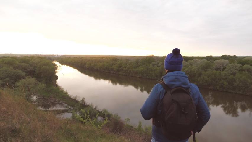 Happy male traveler with a backpack on his shoulders rejoices at the goal having raised his hands and jumping up. A tourist who climbed the mountain and arrived at the destination. A man seeker of a