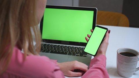 Close up woman using smartphone green screen on the table with laptop computer Chromakey. Close up shot of woman's hands holding mobile phone swiping scrolling green screen..