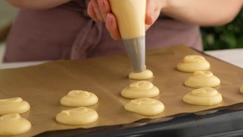 Cooking choux or profiteroles, female hands squeeze the dough from the bag onto baking sheet, general view. Cooking creamy and berry choux with chocolate craquelin. Vanilla choux
