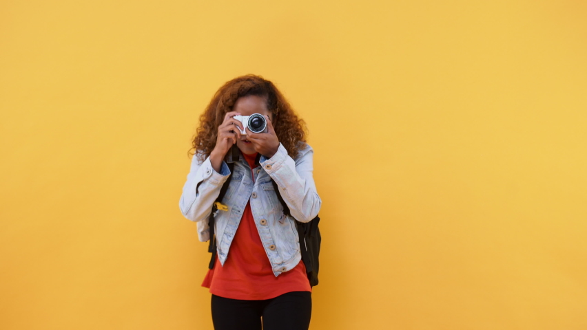 Amazed solo woman tourist taking photo with camera in yellow isolated studio background  