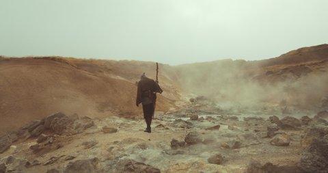 Handheld Slow Motion Wide Shot Of Hooded Man In Robes Carrying Staff Through Mysterious Desert Landscape