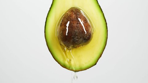 Slow motion close-up of fresh avocado fruit and oil flowing on white background