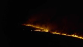 Top view and flying over field with a fire, at night.  Dramatic video shooting, smoke clouds, the spread of fire. Climate change, ecology. Uncontrolled rural  fire. Burning of dry grass