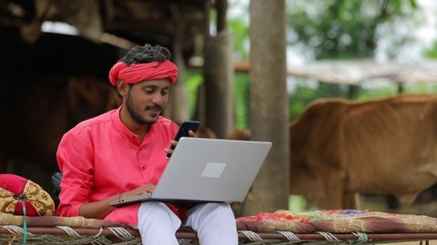 Young indian farmer talking on mobile phone and using laptop at home
