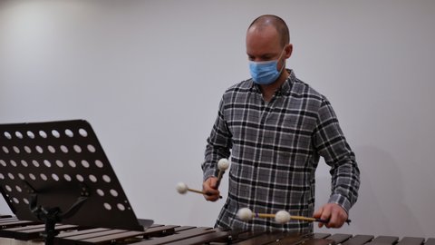 caucasian percussion music teacher professor wearing mask and playing marimba. life after covid pandemic and teacher masked at art school concept. teaching and education during covid concept. learning
