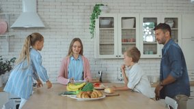 Smiling family talking while serving table during breakfast in kitchen