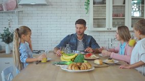 Family drinking juice, eating pancakes and talking during breakfast in kitchen