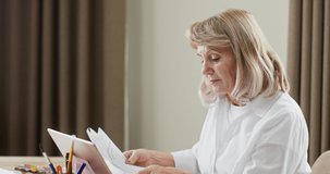 Stressed senior woman doing paperwork or accounts as she sits at a laptop computer pausing to rub her temples and neck with her fingers with a worried expression