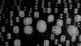 This close up slow motion video shows spray suds on a black surface.