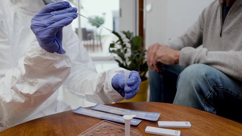 Close up of medical staff hands with gloves introducing the nasal swab to the buffer tube to take a nasal culture sampling from a senior man on a home visit. Rapid Antigen Test for Covid-19.