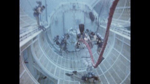 1980s: Scientists in scuba gear and astronauts perform experiments underwater in pool. Plane flies high above clouds. Astronauts perform exercises on plane in near weightlessness.