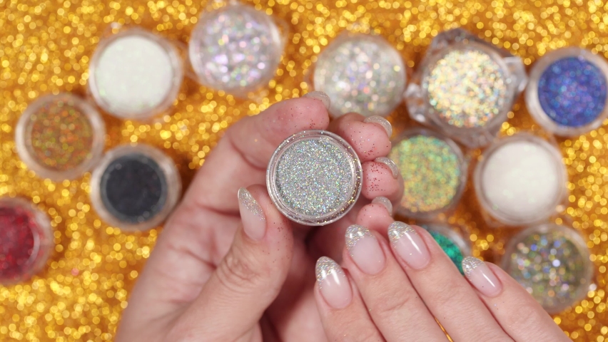Closeup top view 4k video of female hand holding and showing transparent can with bright silver diamond holographic powder for modern trendy naildesign in professional beauty studio or spa salon. 