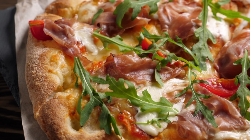 Prosciutto pizza with strachatella cheese, tomatoes and arugula leaves. Rotating on wooden table Royalty-Free Stock Footage #1064496424