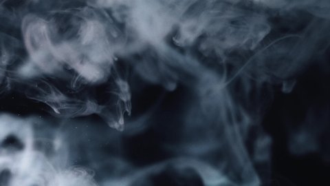 Bright blue paint on a black background moves slowly in the water. Abstract isolated smoke explosion.