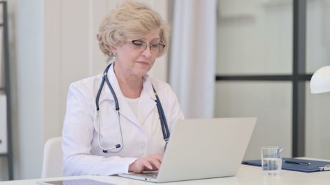 Old Female Doctor Working on Laptop in Clinic 