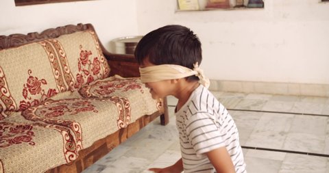 Young boy and girl children playing hide and seek with eyes closed with fabric cloth as they playfully run around each other and the other hand to catch blindfolded in the living room