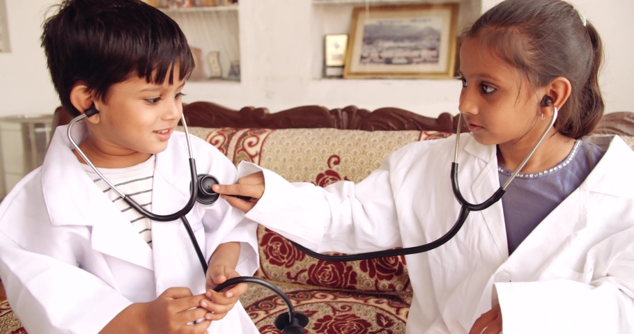 Handheld slow-motion of siblings, boy girl, wearing white doctor lap coat costume with stethoscope to check heart beat, aspire to be health care medical professional medecine to cure illness disease