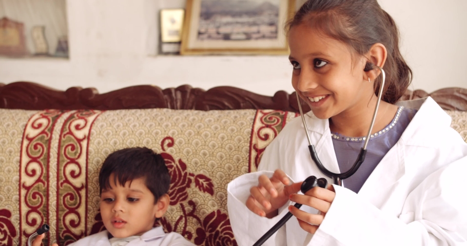 Handheld slow-motion of siblings, boy girl, wearing white doctor lap coat costume with stethoscope to check heart beat, aspire to be health care medical professional medecine to cure illness disease