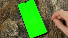 Human Hand Flipping Glides Touches the Green Screen of the Smartphone Background on the Marble Surface, Chroma Key, Alpha Channel. Use Phone to View Video Content, Video  Blog or Surf the Internet