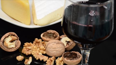 Closeup of a glass of red wine being served, nuts and parmesan and brie (tracking side).