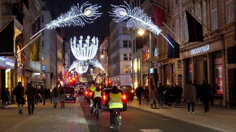 LONDON, ENGLAND, UNITED KINGDOM - CIRCA DECEMBER, 2020: Bicycle riders, cars and pedestrians moving along New Bond Street with illuminated street Christmas decorations at night.