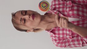 Happy young woman holding swirl lollipop on white background. Beautiful woman with blond hair holding a pink sweet colorful lollipop candy.Video for the vertical story.