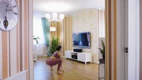 Online fitness workout remotely, at home. Young woman, in sportswear, watching tutorial video with fitness coach on TV and practicing exercises at home. Online workout.