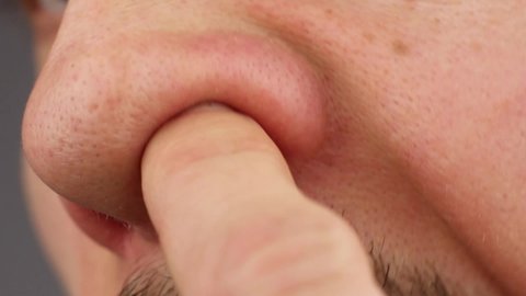 man clean up or picks his right nostril, scratches his itchy nose, loss of smell, close-up side view