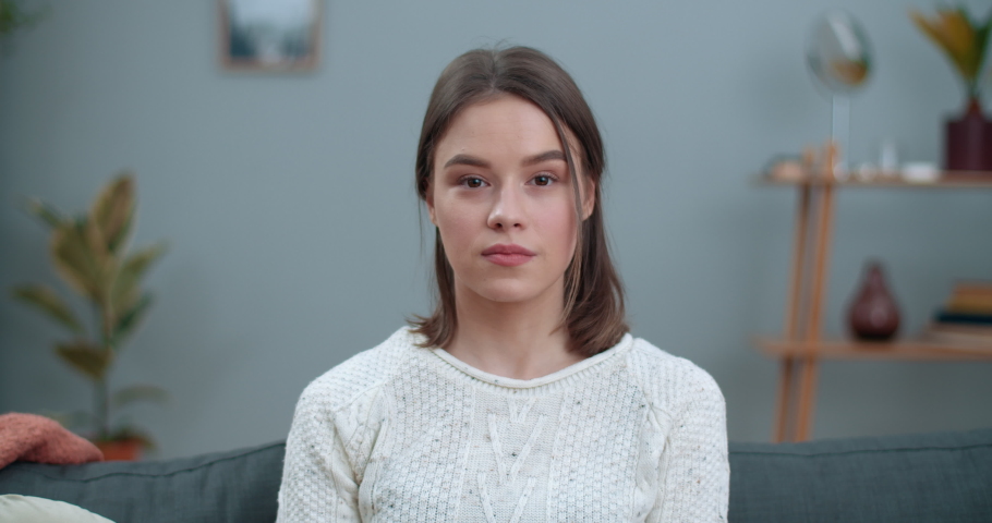 Crop view of millennial woman saying nonverbal phrase I hear it with my heart while sitting on couch. Joyful female person looking to camera and communicating with sign language Royalty-Free Stock Footage #1064542873