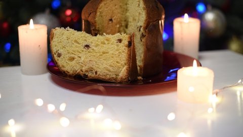 Festive Christmas Italian dessert Panettone on a white table with candles and a garland of light on a bokeh background of a Christmas tree with toys. Festive cooking, new year, delicious, sweets, cozy
