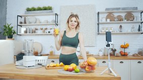 athletic young adult woman fitness coach and blogger, tells online about diet and healthy eating. Slender fit girl records video on a smartphone camera. weight loss training in the kitchen at home